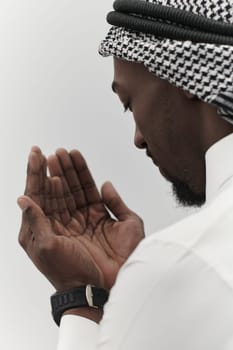African American Muslim man raises his hands in prayer, seeking solace and devotion to God, as he stands isolated against a serene white backdrop, symbolizing a profound expression of faith and contemplation.
