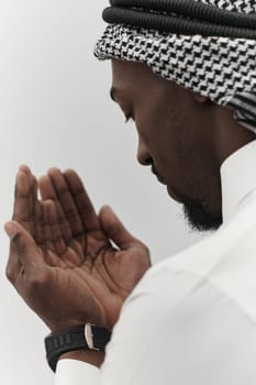 African American Muslim man raises his hands in prayer, seeking solace and devotion to God, as he stands isolated against a serene white backdrop, symbolizing a profound expression of faith and contemplation.