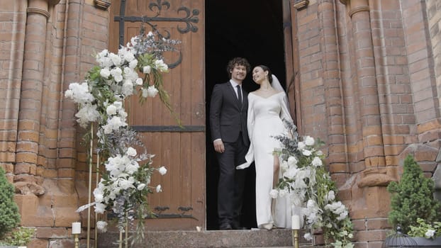 Newlyweds are standing at temple. Action. Beautiful couple of newlyweds stands in doorway of temple. Newlyweds at wedding ceremony at European temple.