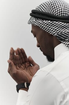 African American Muslim man raises his hands in prayer, seeking solace and devotion to God, as he stands isolated against a serene white backdrop, symbolizing a profound expression of faith and contemplation.