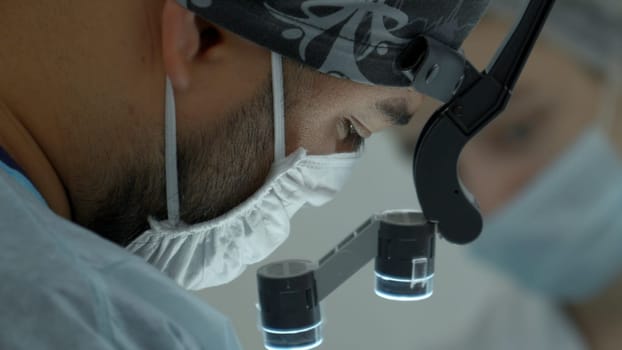 Surgeon head with professional glasses at operating room. Action. Close up side view of a doctor in glasses with binocular magnifiers