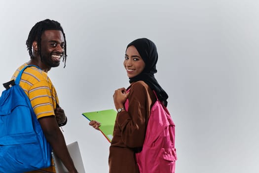 African American student collaborates with his Muslim colleague, who diligently works on her laptop, symbolizing a blend of diversity, modern learning, and cooperative spirit against a serene white background.