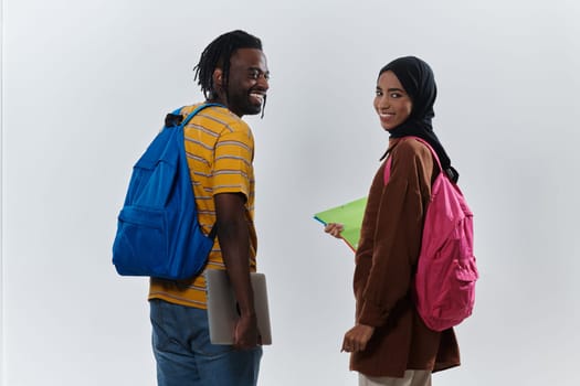 African American student collaborates with his Muslim colleague, who diligently works on her laptop, symbolizing a blend of diversity, modern learning, and cooperative spirit against a serene white background.