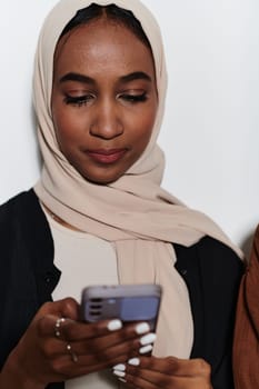 An elegant Arab woman, adorned in a hijab, engages with modernity as she uses a smartphone, the juxtaposition of traditional attire against contemporary technology captured in the isolated setting against a pristine white background.