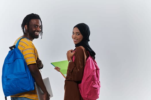 African American student collaborates with his Muslim colleague, who diligently works on her laptop, symbolizing a blend of diversity, modern learning, and cooperative spirit against a serene white background.