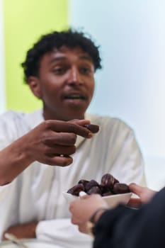 African American Muslim man delicately takes dates to break his fast during the Ramadan month, seated at the family dinner table, embodying a scene of spiritual reflection, cultural tradition, and the shared anticipation of the communal iftar.