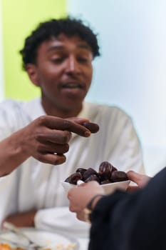 African American Muslim man delicately takes dates to break his fast during the Ramadan month, seated at the family dinner table, embodying a scene of spiritual reflection, cultural tradition, and the shared anticipation of the communal iftar.