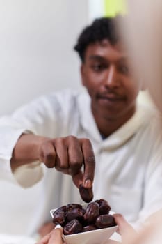 African American Muslim man delicately takes dates to break his fast during the Ramadan month, seated at the family dinner table, embodying a scene of spiritual reflection, cultural tradition, and the shared anticipation of the communal iftar.