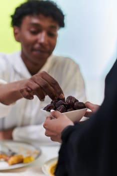 African American Muslim man delicately takes dates to break his fast during the Ramadan month, seated at the family dinner table, embodying a scene of spiritual reflection, cultural tradition, and the shared anticipation of the communal iftar.