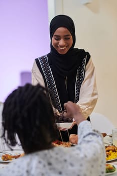 In a heartwarming scene during the sacred month of Ramadan, a traditional Muslim woman offers dates to her family gathered around the table, exemplifying the spirit of unity, generosity, and cultural richness during this festive and spiritual occasion.