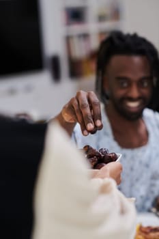 African American Muslim man delicately takes dates to break his fast during the Ramadan month, seated at the family dinner table, embodying a scene of spiritual reflection, cultural tradition, and the shared anticipation of the communal iftar.