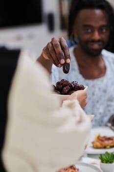 African American Muslim man delicately takes dates to break his fast during the Ramadan month, seated at the family dinner table, embodying a scene of spiritual reflection, cultural tradition, and the shared anticipation of the communal iftar.