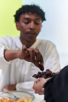 African American Muslim man delicately takes dates to break his fast during the Ramadan month, seated at the family dinner table, embodying a scene of spiritual reflection, cultural tradition, and the shared anticipation of the communal iftar.