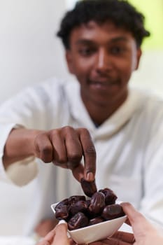 African American Muslim man delicately takes dates to break his fast during the Ramadan month, seated at the family dinner table, embodying a scene of spiritual reflection, cultural tradition, and the shared anticipation of the communal iftar.