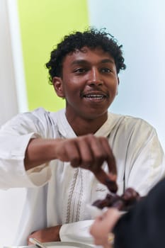 African American Muslim man delicately takes dates to break his fast during the Ramadan month, seated at the family dinner table, embodying a scene of spiritual reflection, cultural tradition, and the shared anticipation of the communal iftar.