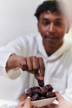 African American Muslim man delicately takes dates to break his fast during the Ramadan month, seated at the family dinner table, embodying a scene of spiritual reflection, cultural tradition, and the shared anticipation of the communal iftar.