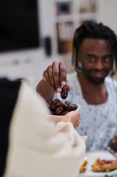 African American Muslim man delicately takes dates to break his fast during the Ramadan month, seated at the family dinner table, embodying a scene of spiritual reflection, cultural tradition, and the shared anticipation of the communal iftar.