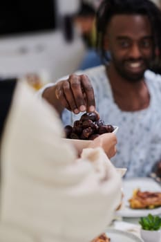 African American Muslim man delicately takes dates to break his fast during the Ramadan month, seated at the family dinner table, embodying a scene of spiritual reflection, cultural tradition, and the shared anticipation of the communal iftar.