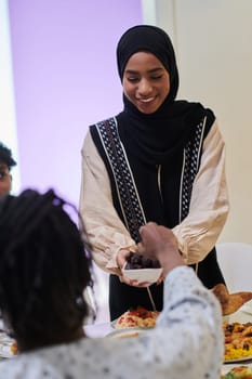 In a heartwarming scene during the sacred month of Ramadan, a traditional Muslim woman offers dates to her family gathered around the table, exemplifying the spirit of unity, generosity, and cultural richness during this festive and spiritual occasion.