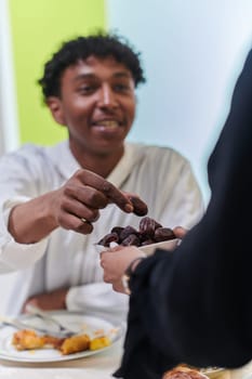 African American Muslim man delicately takes dates to break his fast during the Ramadan month, seated at the family dinner table, embodying a scene of spiritual reflection, cultural tradition, and the shared anticipation of the communal iftar.