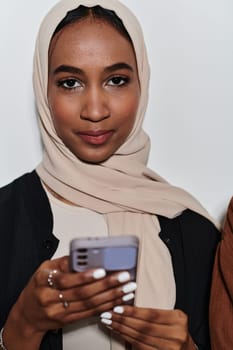 An elegant Arab woman, adorned in a hijab, engages with modernity as she uses a smartphone, the juxtaposition of traditional attire against contemporary technology captured in the isolated setting against a pristine white background.