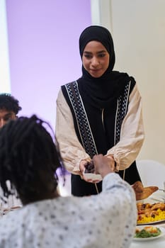 In a heartwarming scene during the sacred month of Ramadan, a traditional Muslim woman offers dates to her family gathered around the table, exemplifying the spirit of unity, generosity, and cultural richness during this festive and spiritual occasion.
