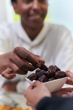 African American Muslim man delicately takes dates to break his fast during the Ramadan month, seated at the family dinner table, embodying a scene of spiritual reflection, cultural tradition, and the shared anticipation of the communal iftar.