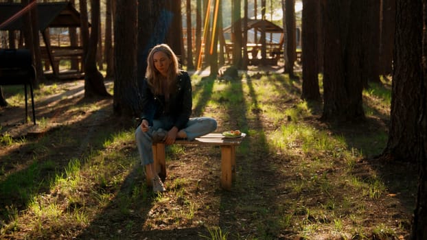 Beautiful blonde woman near wooden pavilions in the summer forest. Stock footage. Woman enjoying nature alone