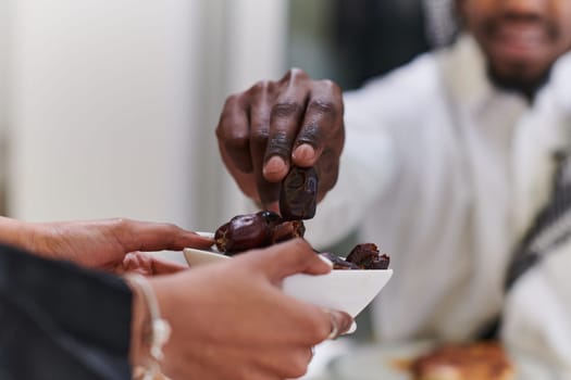 African American Muslim man delicately takes dates to break his fast during the Ramadan month, seated at the family dinner table, embodying a scene of spiritual reflection, cultural tradition, and the shared anticipation of the communal iftar.