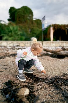 Little girl squats on the beach and touches a stone with her hand. High quality photo