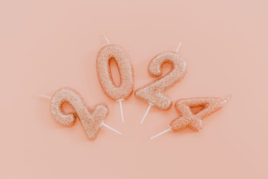 Shiny candle numbers 2024 lie in a semicircle in the center on a pink background, flat lay close-up.