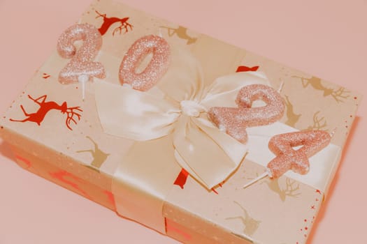Shiny candles with the number 2024 on a gift box tied with a bow lie diagonally on a pink background, close-up side view.