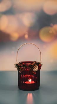 One red Christmas glass jar with a candle burning in it stands on a blurred colorful background with bokke and copy space from above, side view close-up.
