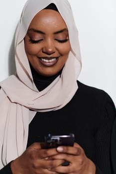 An elegant Arab woman, adorned in a hijab, engages with modernity as she uses a smartphone, the juxtaposition of traditional attire against contemporary technology captured in the isolated setting against a pristine white background.