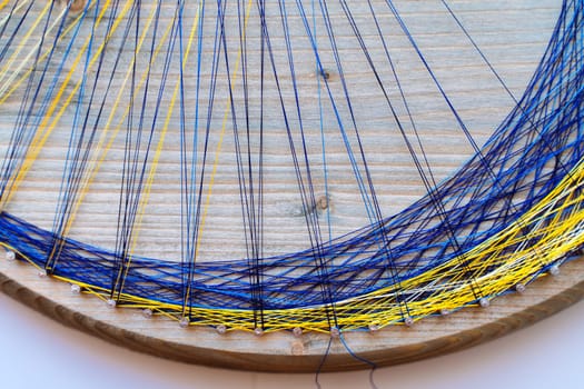 Colored thread mandala on a wooden board with nails. Mandala Moon Harmony Sun esotericism and psychology pictures from yellow and blue silk threads