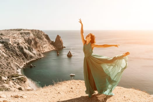 Woman green dress sea. Female dancer posing on a rocky outcrop high above the sea. Girl on the nature on blue sky background. Fashion photo