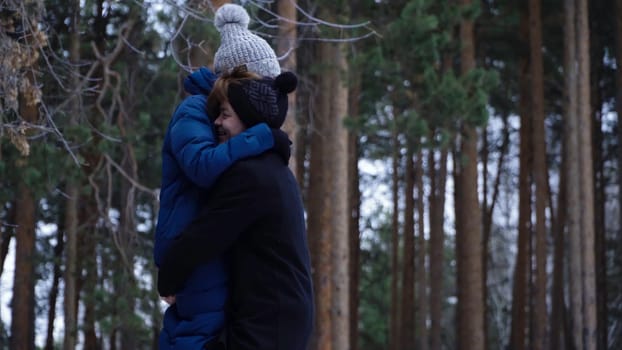 Young couple hugging and kissing in park in winter. Couple happy together. Young man circling his girlfriend in arms against winter forest.