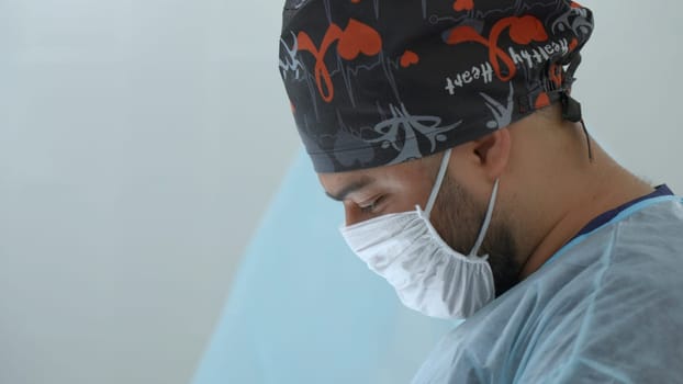 A close up male medical worker with a disposable mask and hat. Action. Surgeon at work in modern clinic