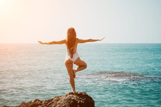 Woman sea yoga. Back view of free calm happy satisfied woman with long hair standing on top rock with yoga position against of sky by the sea. Healthy lifestyle outdoors in nature, fitness concept