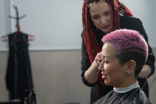 The hairdresser shaves the temple of a female client. Asian woman with short pink hair in barbershop