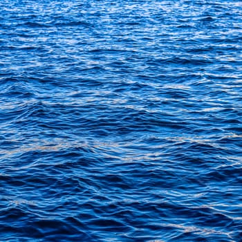 Blue sea waves in sunshine glow as surface background. Summer holidays and coastal nature concept