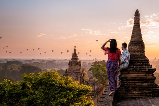 Bagan Myanmar, a couple of men and women are looking at the sunrise on top of an old pagoda temple. a couple on vacation in Myanmar Asia visit the historical site of Bagan with hot air balloons