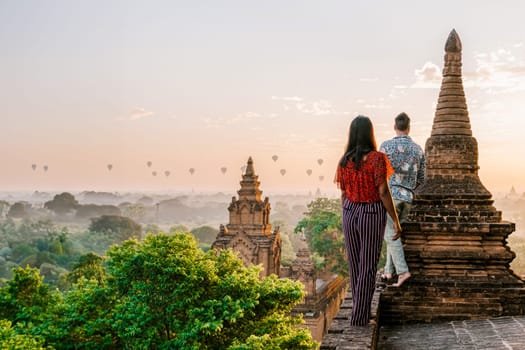 Bagan Myanmar, a couple of men and women are looking at the sunrise on top of an old pagoda temple. a couple watching sunrise with hot air balloons in the sky in Myanmar Asia Bagan