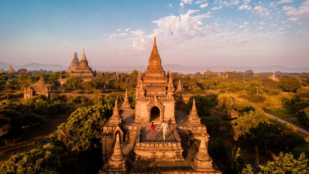 Bagan Myanmar, a couple of men and women are looking at the sunrise on top of an old pagoda temple.