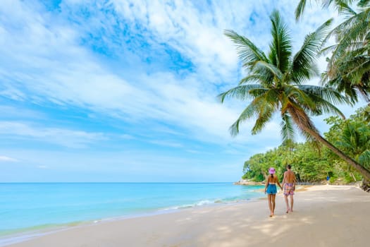 Phuket Thailand, a couple of men and woman walking at the beach of Surin, Surin Beach Phuket. A couple walking on a tropical beach with palm trees