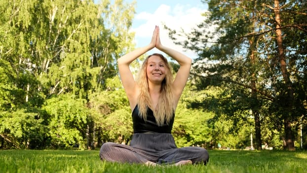 Yoga in a bright green clearing. Concept. A young beautiful woman with long curly hair who dances in a lotus pose against a background of green trees and sunlight. High quality 4k footage