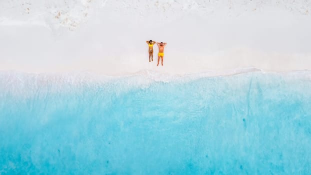 Drone top view of a couple of men and women lying down on the beach of Small Curacao Island, a couple relaxing on the beach of Curacao, top view at a tropical beach