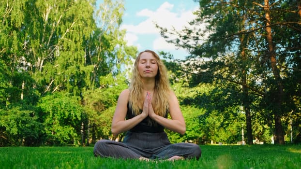 Beautiful young woman meditating in park. Concept. Bright young woman does yoga in green park. Woman meditates on grass in right on summer day.