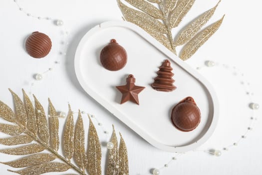 Chocolate in the shape of Christmas tree toys on a white background with elements of Christmas decorations. A postcard for the New Year