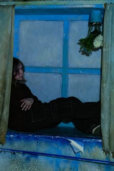 The concept of sad depression of a teenage girl. A frustrated teenage girl is sitting on a windowsill in an old sad room